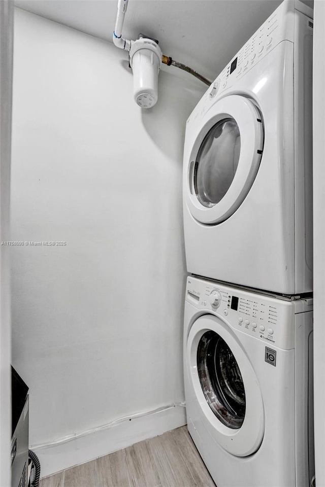 laundry room featuring laundry area, baseboards, wood finished floors, and stacked washer and clothes dryer