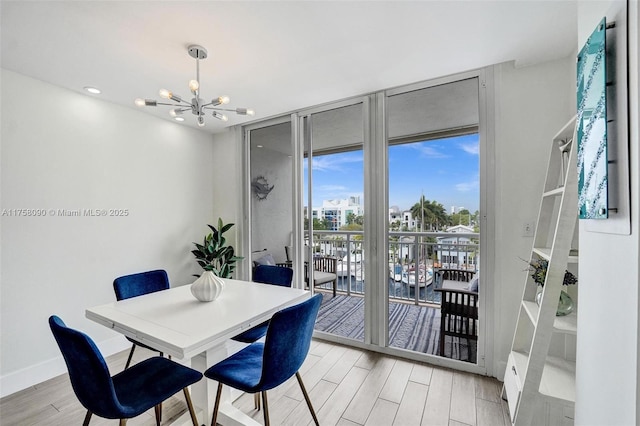 dining room featuring a chandelier, light wood finished floors, a wall of windows, and baseboards