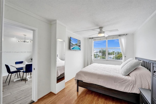 bedroom with ornamental molding, light wood finished floors, a textured ceiling, and ceiling fan with notable chandelier