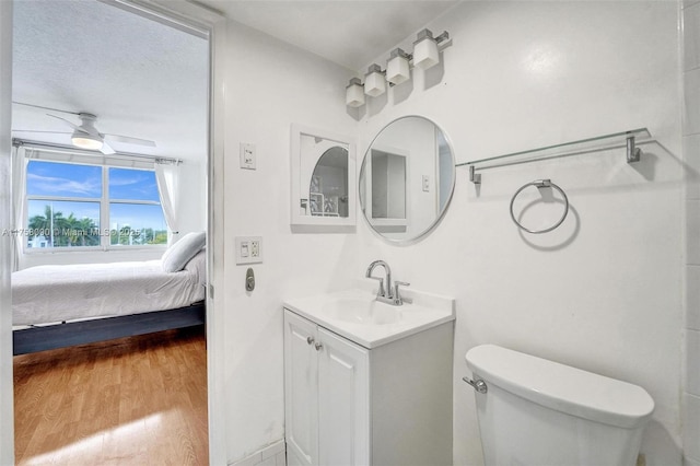 ensuite bathroom with ceiling fan, toilet, wood finished floors, vanity, and ensuite bath