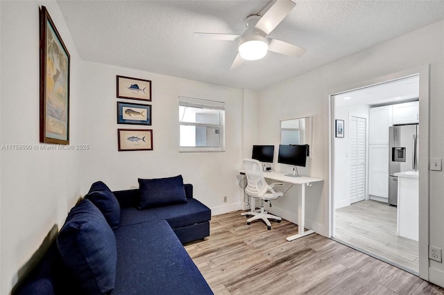 home office with light wood-type flooring, ceiling fan, baseboards, and a textured ceiling