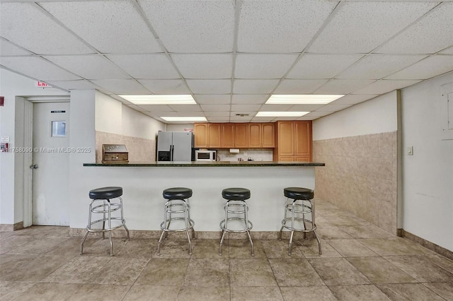 kitchen with stainless steel appliances, dark countertops, brown cabinetry, and a breakfast bar area