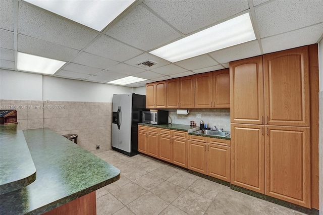 kitchen featuring visible vents, brown cabinetry, dark countertops, stainless steel appliances, and a sink