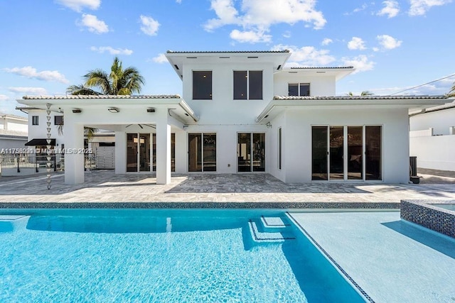 rear view of property featuring a patio area, stucco siding, an outdoor pool, and a tiled roof