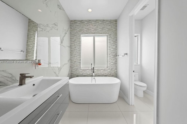 bathroom with tile walls, a soaking tub, vanity, and toilet