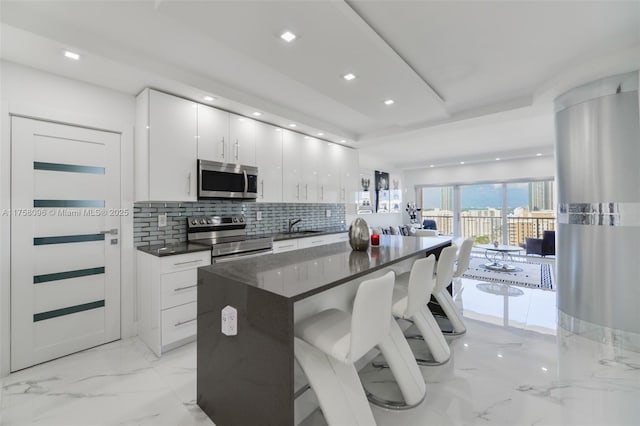 kitchen featuring a breakfast bar, marble finish floor, tasteful backsplash, dark countertops, and appliances with stainless steel finishes