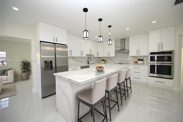 kitchen featuring visible vents, a breakfast bar, stainless steel appliances, decorative backsplash, and wall chimney range hood