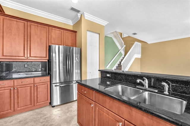 kitchen featuring a sink, backsplash, freestanding refrigerator, brown cabinets, and dark stone countertops