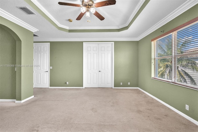 unfurnished bedroom featuring arched walkways, a tray ceiling, carpet, and visible vents