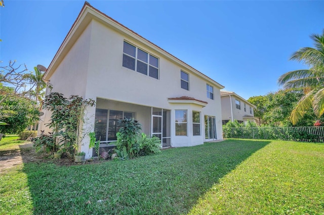 rear view of property featuring stucco siding, fence, a sunroom, and a yard