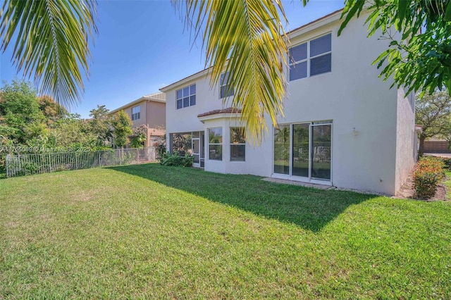 rear view of property featuring a lawn, fence, and stucco siding