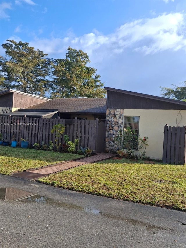 view of property exterior with a yard, stone siding, and fence