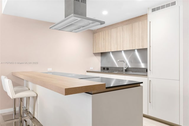 kitchen featuring a breakfast bar area, a peninsula, a sink, range hood, and modern cabinets