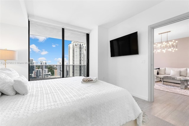 bedroom with a chandelier, wood finished floors, baseboards, access to exterior, and expansive windows