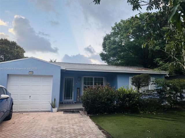 ranch-style house with a front lawn, decorative driveway, an attached garage, and stucco siding