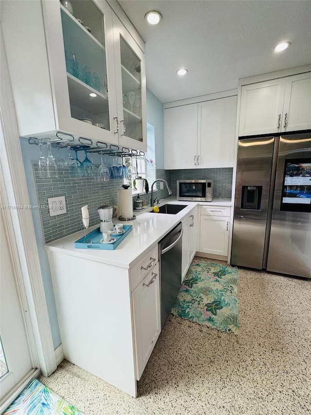 kitchen with glass insert cabinets, stainless steel appliances, light countertops, white cabinetry, and light speckled floor