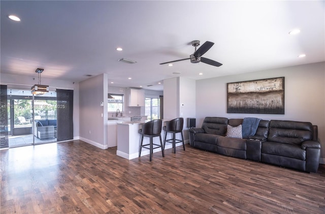 living room featuring plenty of natural light, baseboards, dark wood finished floors, and a ceiling fan