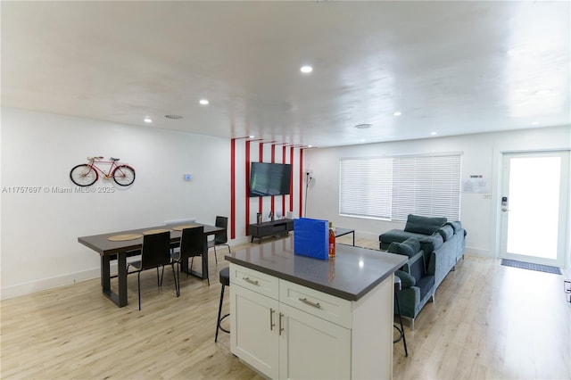 kitchen featuring a breakfast bar area, dark countertops, white cabinetry, and light wood-style floors