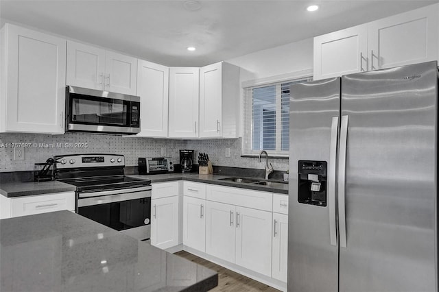 kitchen featuring dark stone counters, stainless steel appliances, a sink, and white cabinetry