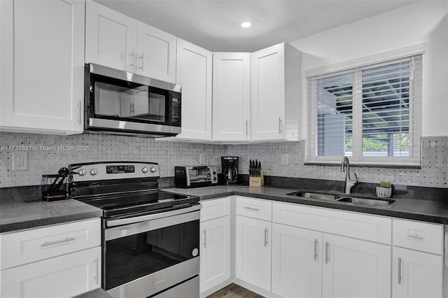 kitchen with a sink, white cabinets, appliances with stainless steel finishes, tasteful backsplash, and dark countertops