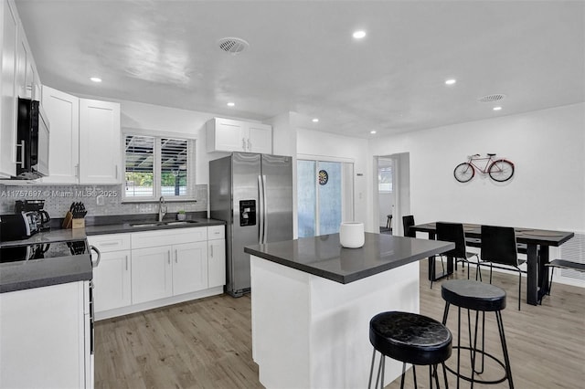 kitchen with a breakfast bar area, a sink, appliances with stainless steel finishes, light wood-type flooring, and dark countertops