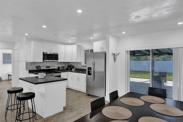 kitchen featuring stainless steel appliances, white cabinetry, backsplash, light wood finished floors, and dark countertops