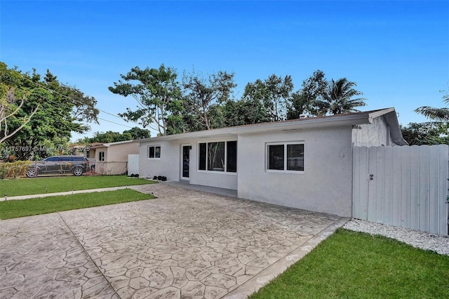 back of house with fence, a yard, a gate, stucco siding, and a patio area