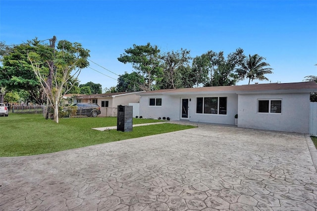 rear view of house with stucco siding, a patio area, fence, and a yard