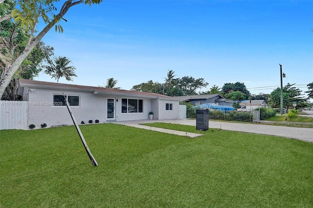 rear view of property with fence, a lawn, and stucco siding