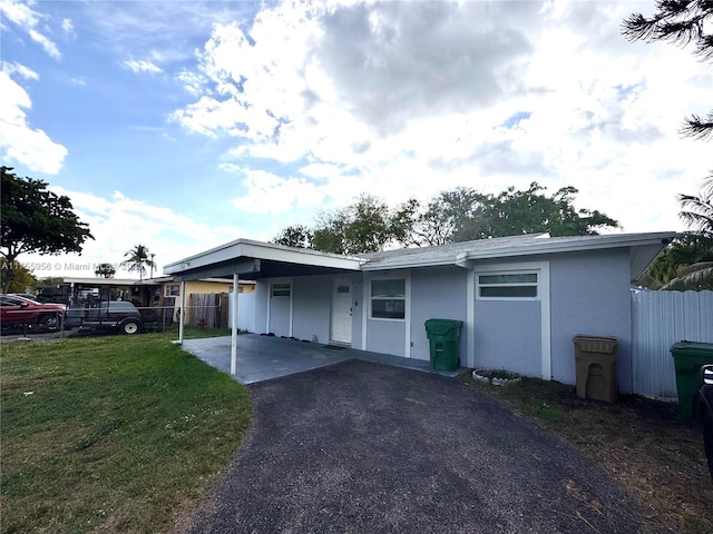 view of front of home with aphalt driveway, an attached carport, a front yard, and fence