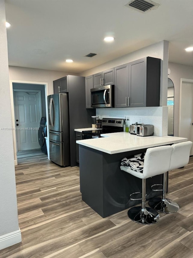 kitchen with light wood-type flooring, independent washer and dryer, appliances with stainless steel finishes, a breakfast bar area, and a peninsula