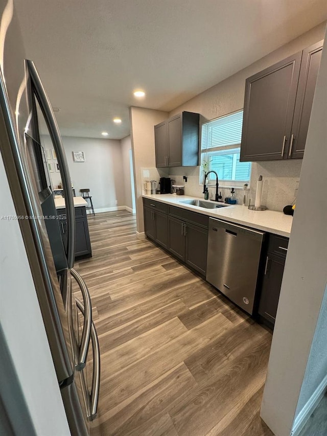 kitchen featuring light wood-type flooring, a sink, tasteful backsplash, stainless steel dishwasher, and light countertops