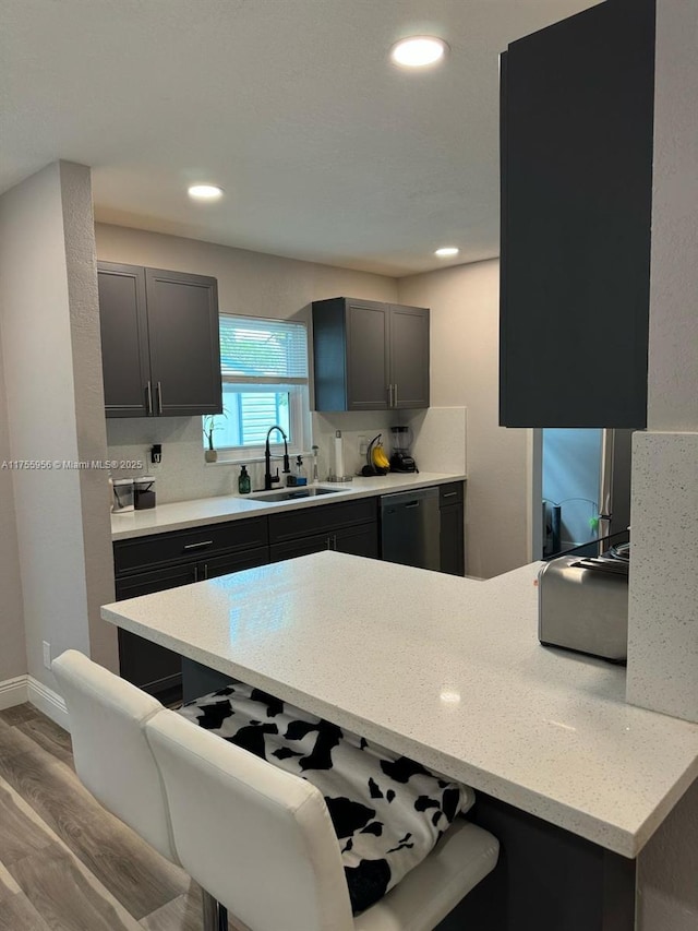 kitchen with wood finished floors, dishwasher, a breakfast bar, and a sink