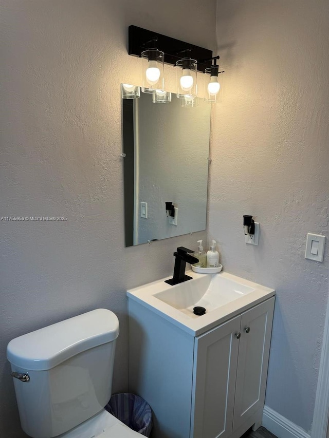 half bathroom with toilet, vanity, and a textured wall