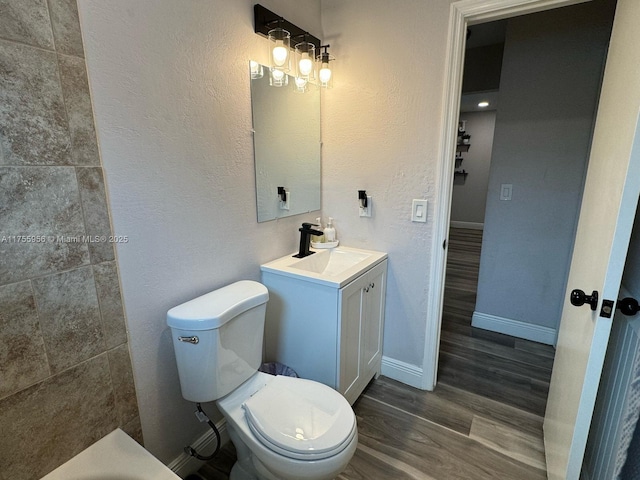 bathroom with toilet, wood finished floors, baseboards, vanity, and a textured wall