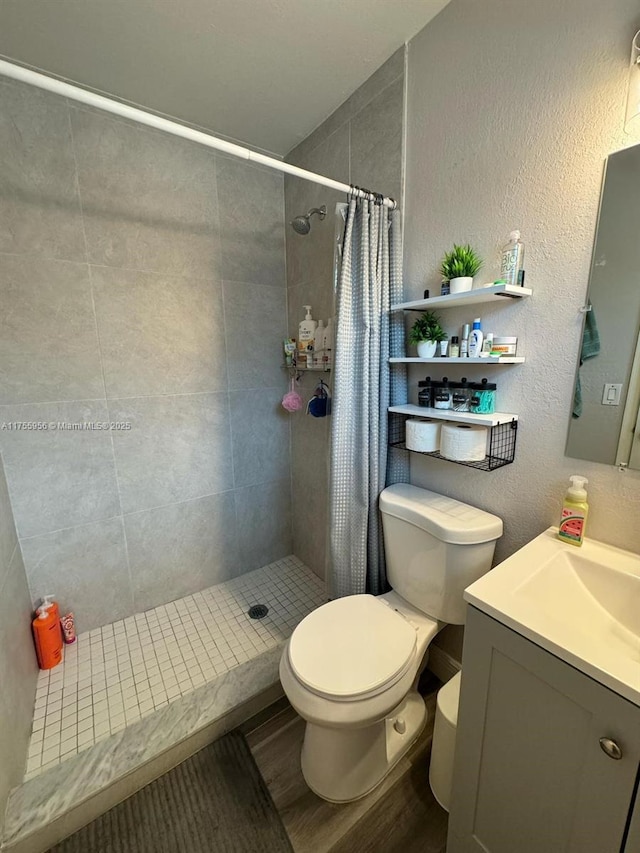 full bath featuring a textured wall, toilet, wood finished floors, and a tile shower