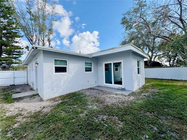 back of house with stucco siding, a yard, and a fenced backyard