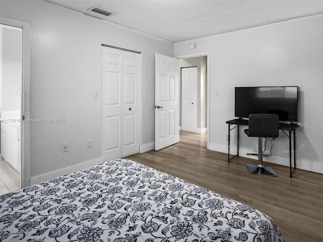 bedroom featuring a textured ceiling, wood finished floors, visible vents, and baseboards