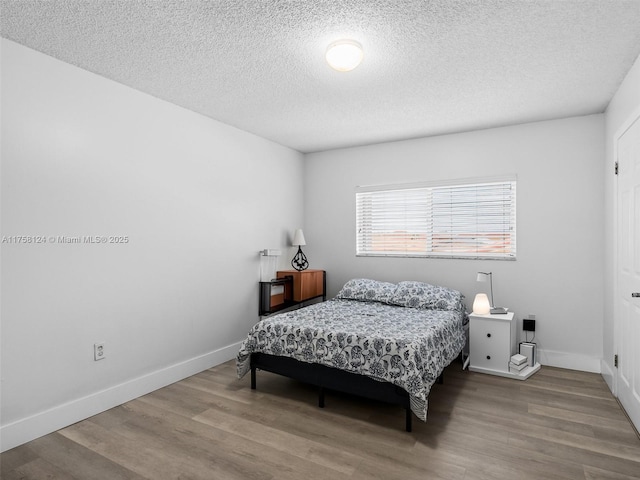 bedroom featuring a textured ceiling, wood finished floors, and baseboards