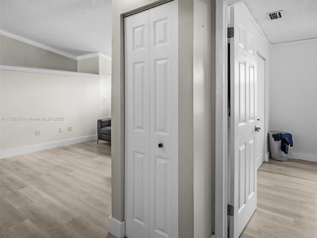 corridor featuring baseboards, visible vents, ornamental molding, wood finished floors, and a textured ceiling