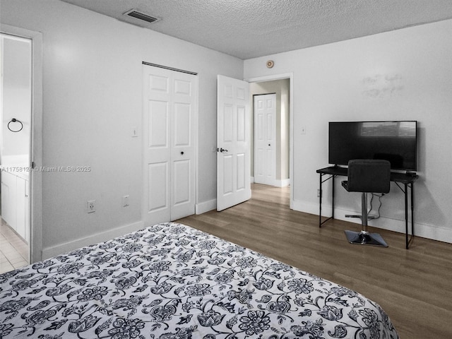 bedroom featuring a closet, visible vents, a textured ceiling, wood finished floors, and baseboards