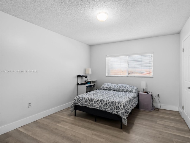 bedroom with a textured ceiling, wood finished floors, and baseboards