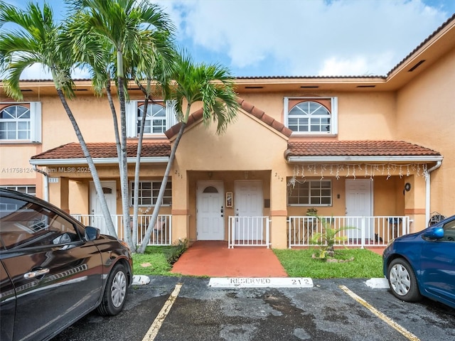 townhome / multi-family property featuring uncovered parking, covered porch, a tile roof, and stucco siding