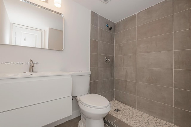 bathroom featuring toilet, a tile shower, and vanity