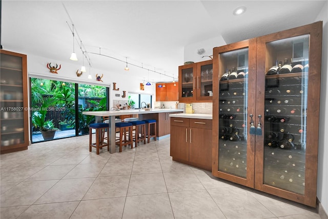 kitchen with light tile patterned floors, light countertops, brown cabinetry, and glass insert cabinets