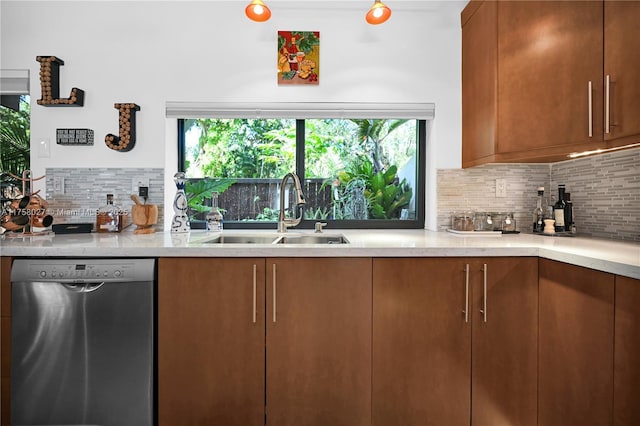 kitchen with light stone counters, backsplash, brown cabinetry, a sink, and dishwasher