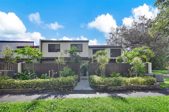 modern home with central air condition unit, a fenced front yard, and stucco siding