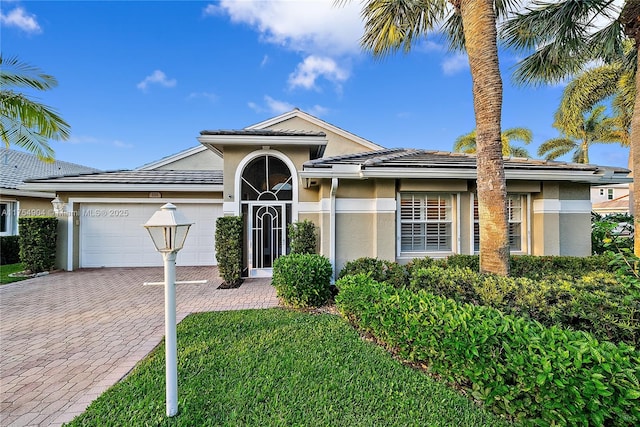 view of front of home featuring a garage, a front lawn, decorative driveway, and stucco siding