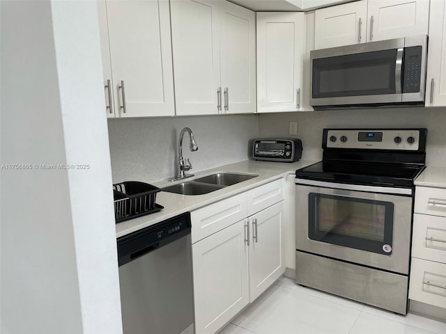 kitchen with appliances with stainless steel finishes, light countertops, a sink, and white cabinetry