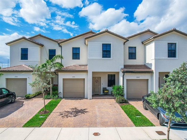 multi unit property with a garage, a tile roof, driveway, and stucco siding